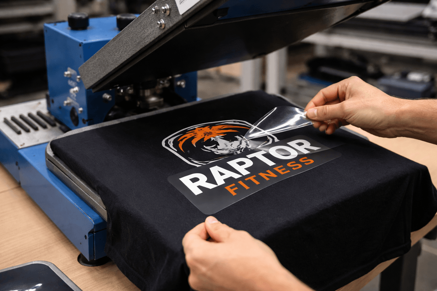 Hands peeling clear film from a Raptor Fitness logo on a black t-shirt.