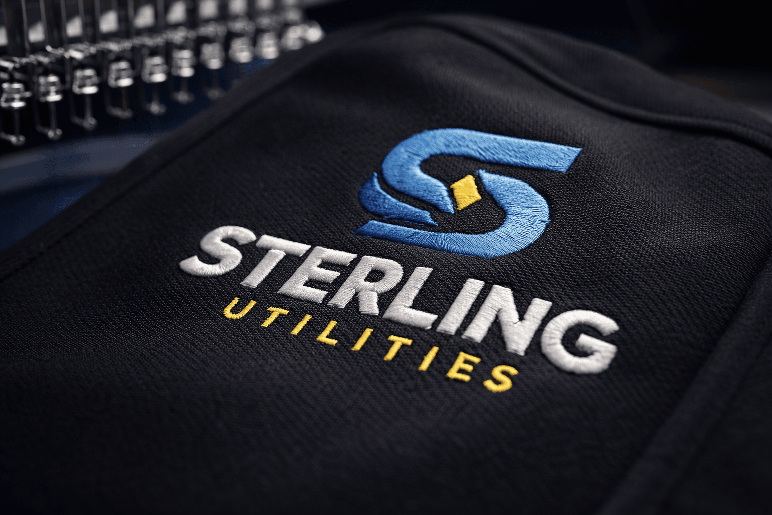 Embroidered Sterling Utilities logo on black fabric with a blurred embroidery machine in the background.
