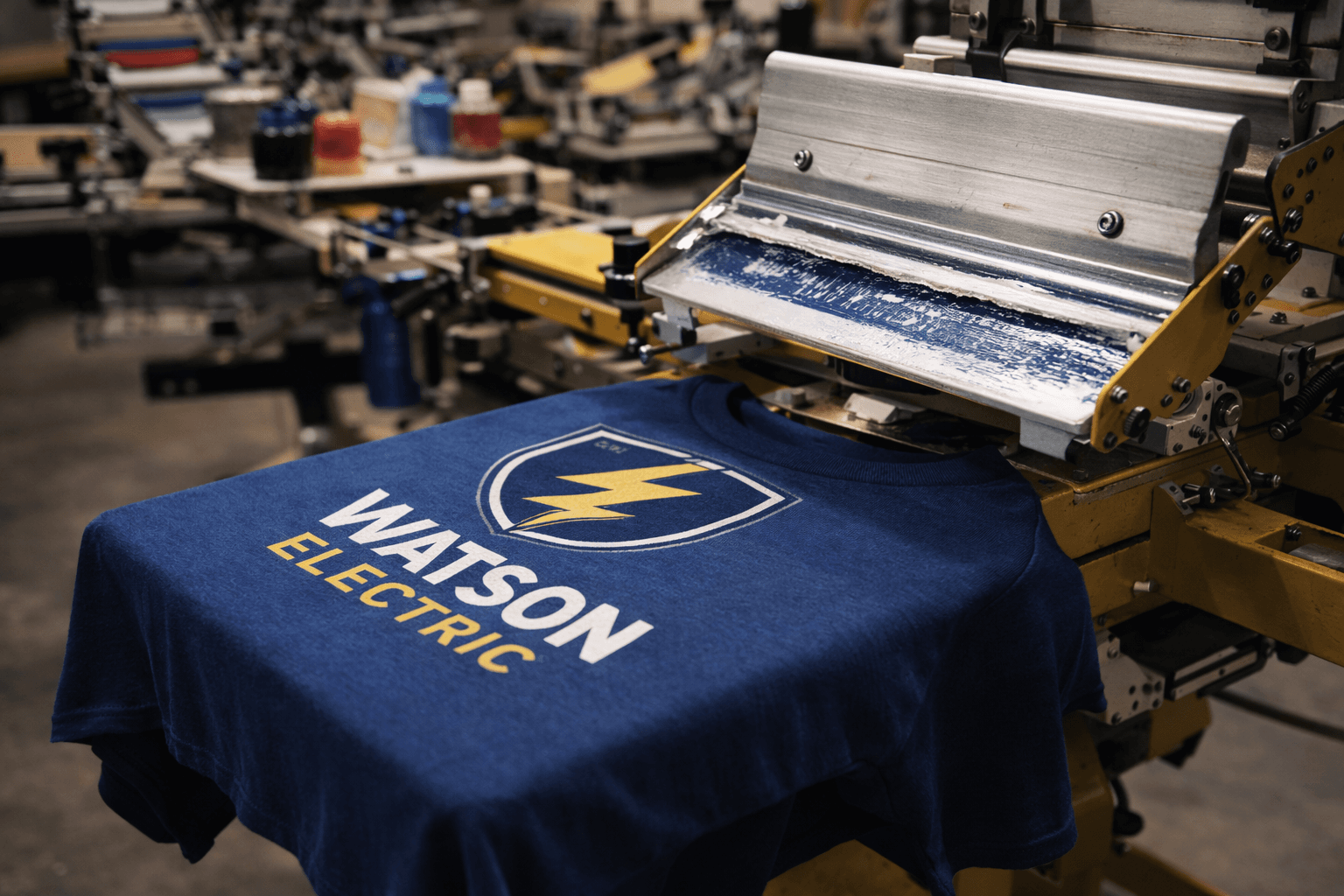 Blue Watson Electric T-shirt with yellow lightning bolt logo on a screen printing machine.